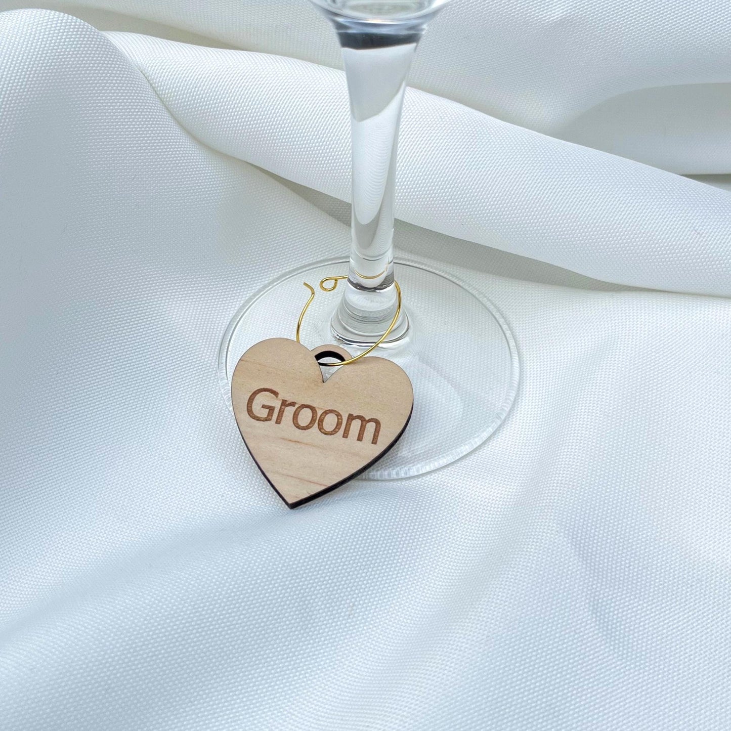 Heart-shaped wooden personalized wine charms tag with Groom text hanging on wine glass stem